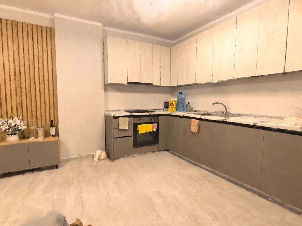 A corner kitchen with grey cabinets and a wooden slat panel in a 3D tour filmed on a phone by lamplight