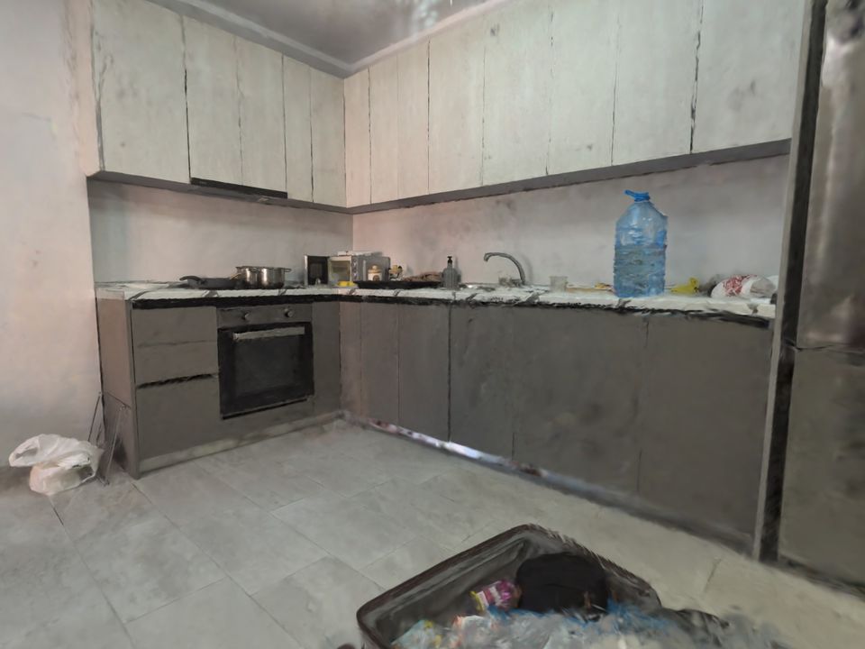 The same kitchen in a 3D tour in daylight: oven, sink, a bottle of water on the counter, an open suitcase in front